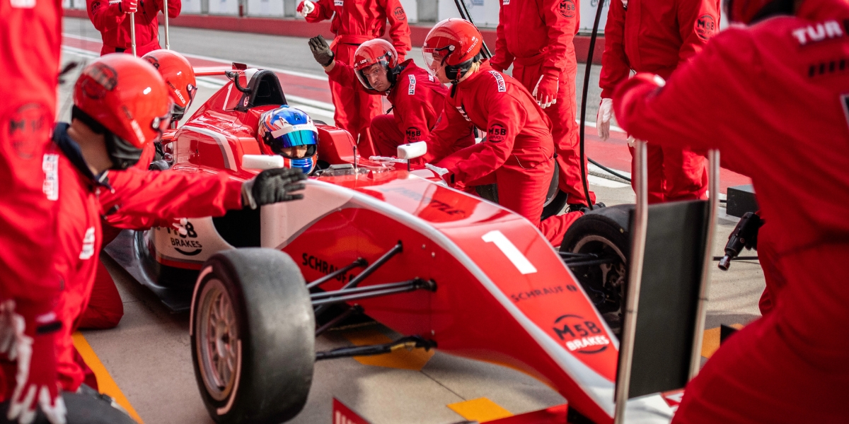 A red race car featuring solvent printed and cut graphics in a pitlane attended by mechanics