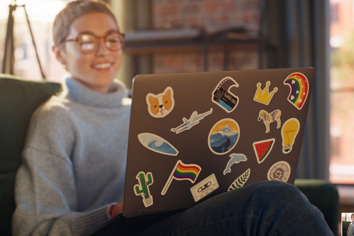 A person using a laptop that has its lid covered with stickers